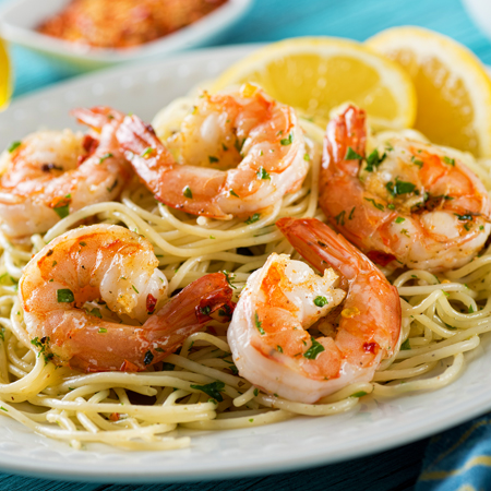 Spot shrimp scampi on a large bed of noodles with lemon slices.