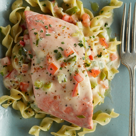 A delicious sockeye salmon fillet on a bed of pasta with a medley sauce poured over top