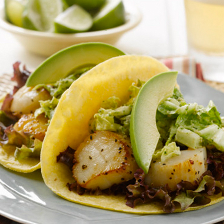 Two tacos filled with scallops & slaw topped with avocado slices