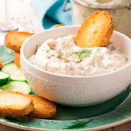 A bowl filled with salmon dip with crackers & cucumber slices