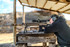 Man shooting a suppressed PRI Mark 12 Mod 0 Gen II rifle mounted with Nightforce Optics NX6 2-12x42mm on tan 1.54 Ultramount from a bench at a shooting range with smoke rising for the muzzle (C730, C729).