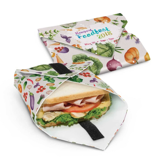 A reusable food wrap featuring a colourful fruit and vegetable design, with a sandwich neatly wrapped inside.