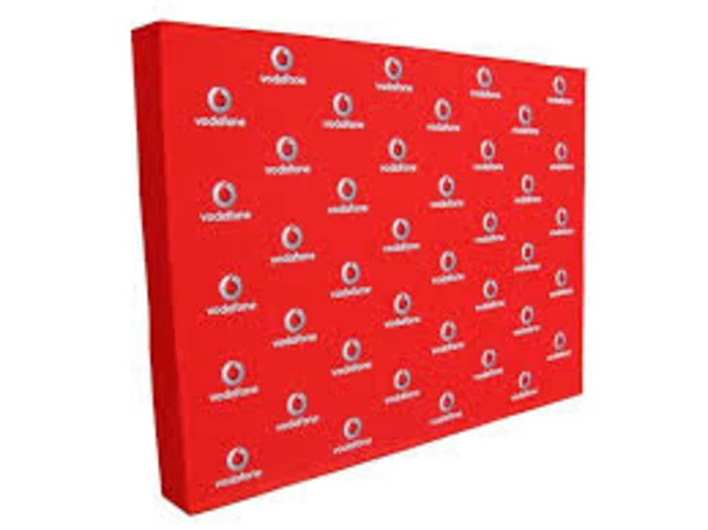 A promotional media wall in bright red, featuring a repeating logo pattern.