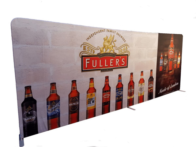 A tension fabric display featuring various beer bottles against a brick wall background, with a prominent logo and branding.