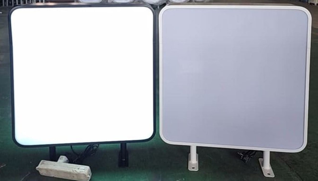 Two wall mount light boxes, one with a black frame and illuminated, the other with a white frame and unlit.