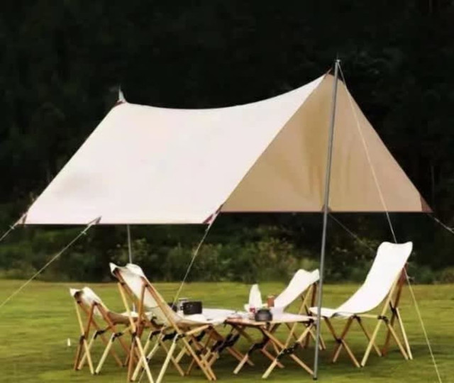 A beige camping canopy with poles set up outdoors, surrounded by wooden folding chairs on green grass.