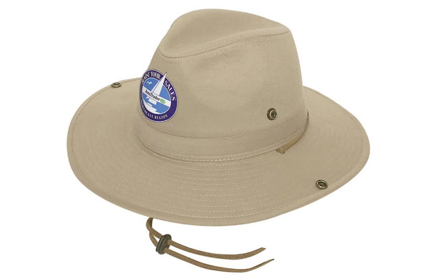 A beige cotton twill hat with a wide brim and a decorative logo. Features a chin strap and metal eyelets.