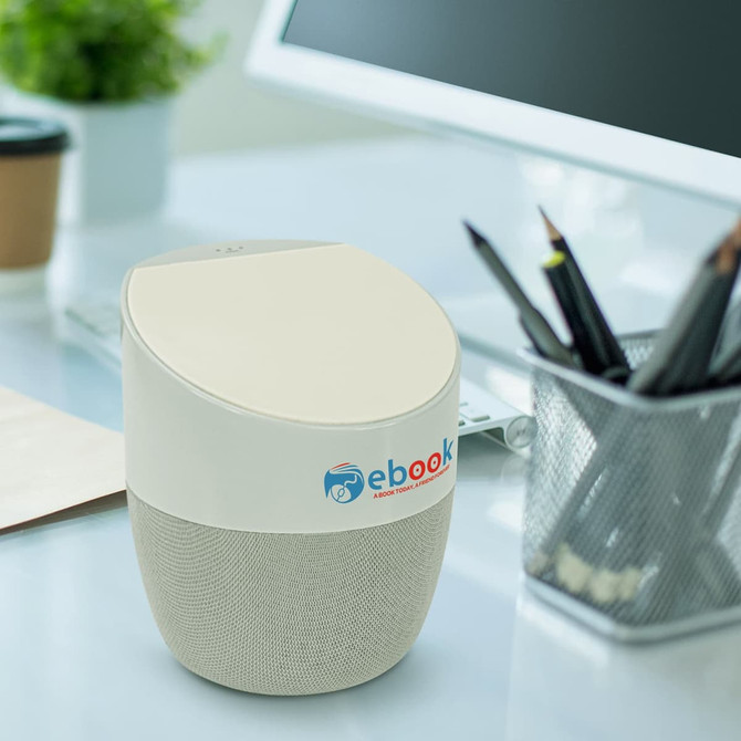 A wireless charger in cream and beige, shaped like a speaker, placed on a desk with a computer and stationery.