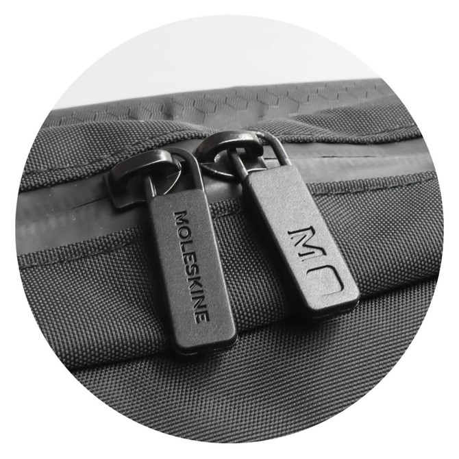 A zip detail of a black Moleskine Metro Slim Backpack featuring dual zippers and a textured surface.