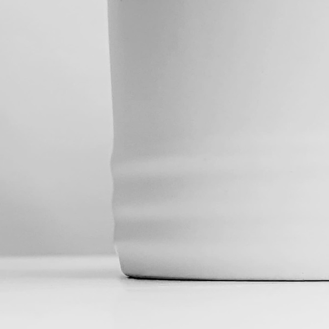 A white coffee mug with a smooth finish and subtle ribbed detailing at the base.