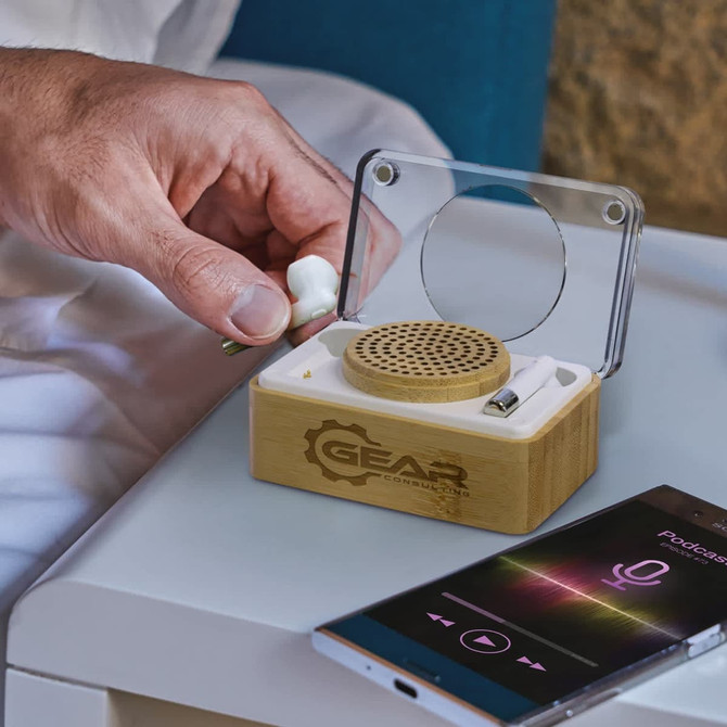 A bamboo wireless speaker and earbud set with a transparent lid and a smartphone displaying audio playback.