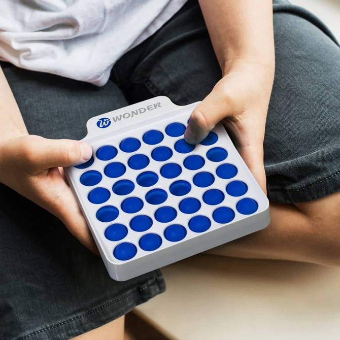 A square fidget popper board with blue buttons on a white base, held in hands.