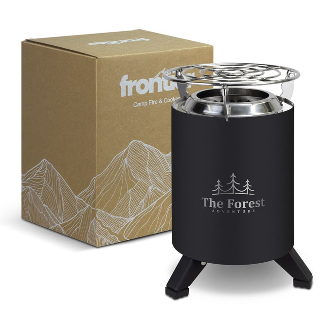 A black camp fire and cooker with a metal top, alongside a cardboard box featuring mountain designs.