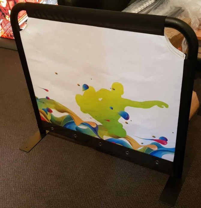 A café barrier featuring a vibrant illustration with green and blue designs, set in a sturdy black frame.