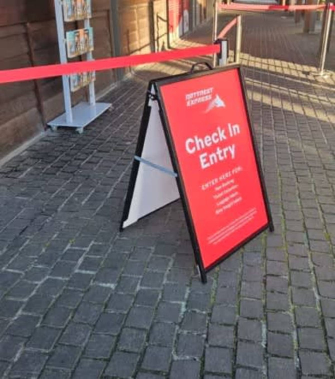 A-frame sign with a red background, featuring a logo and instructions for check-in entry. The frame is black.