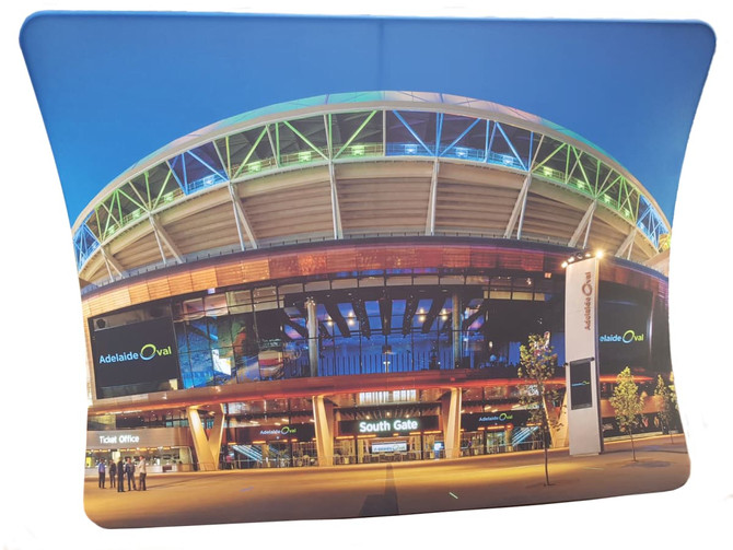A large U-shaped fabric display featuring a vibrant image of Adelaide Oval lit up at night, with a prominent branding logo.