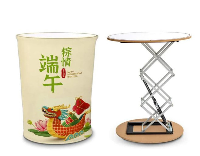 A promotional hydraulic table in a round shape, featuring a white top and a colourful, festive design on the base.
