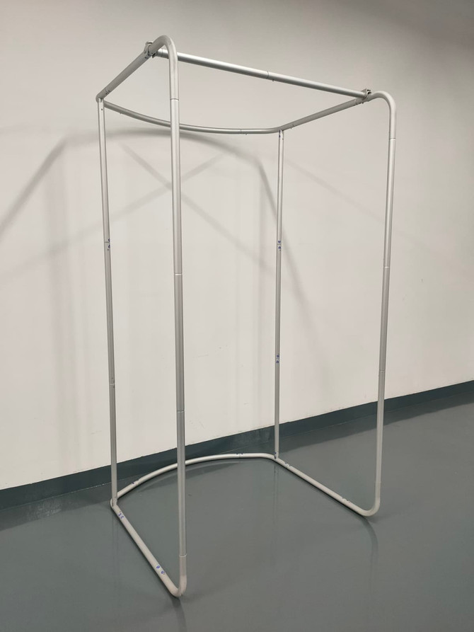 A silver tension fabric change room frame with a rectangular base and open top, set against a plain wall.