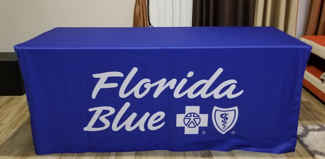 A blue fitted table cover with white branding and logos. Suitable for an 8-foot table.