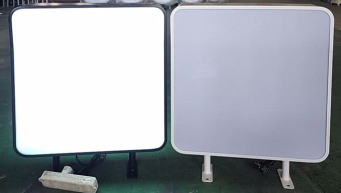 Two wall mount light boxes, one with a black frame and illuminated, the other with a white frame and unlit.