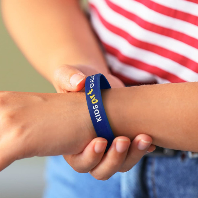 A blue silicone wristband is being worn on a child's wrist, featuring a logo.