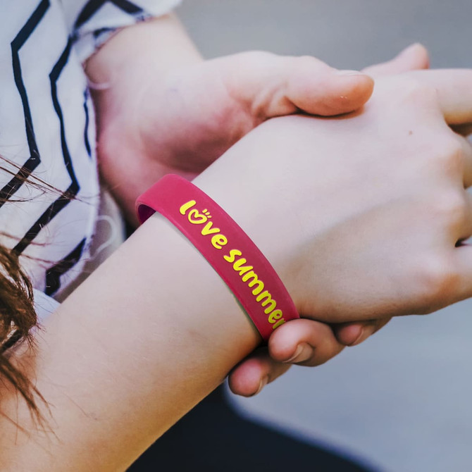 A pink silicone wristband with embossed text and a logo, worn on a person's wrist.
