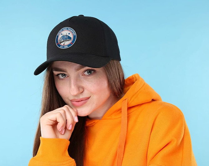 A woman wearing a black cotton twill cap with a buckle, paired with an orange hoodie. The cap features a logo.