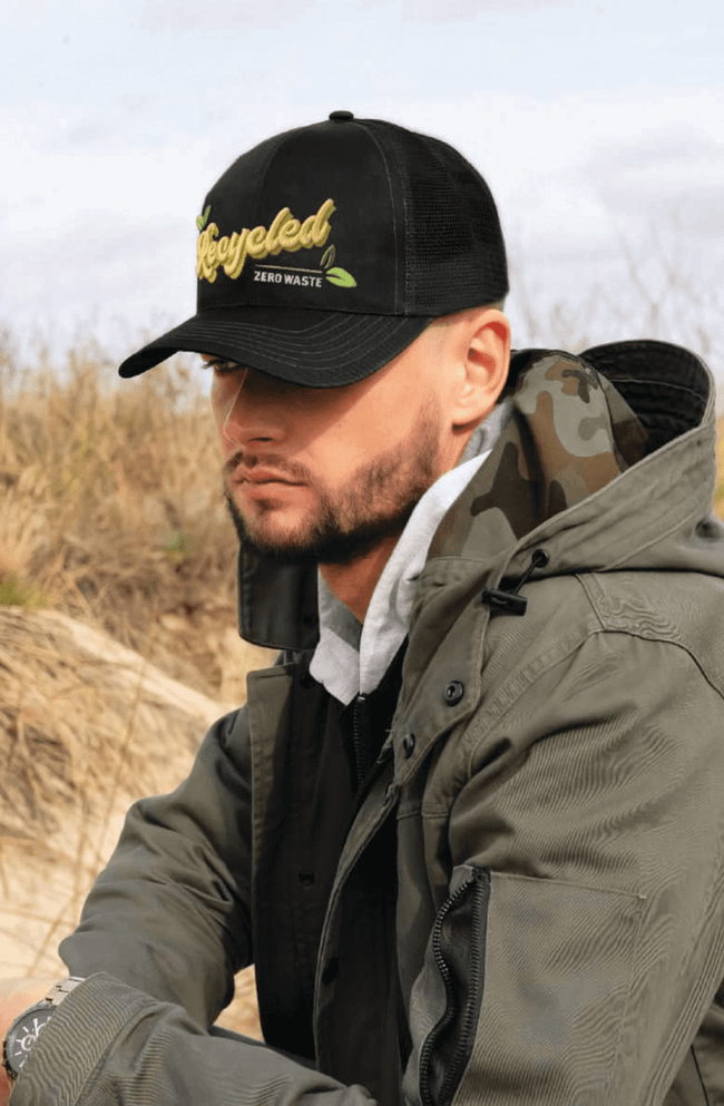 A black cap with a mesh back features a logo and is worn by a person in a green jacket outdoors.