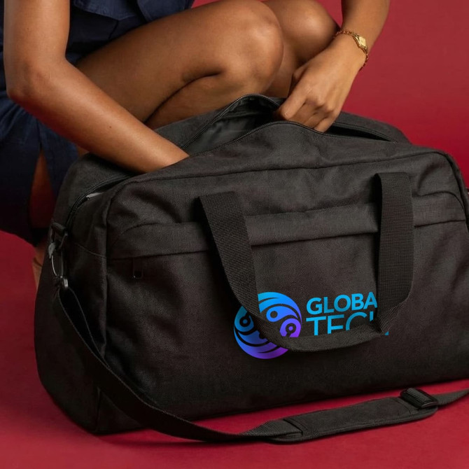 A black duffle bag with handles and a logo, held by a person, set against a red background.