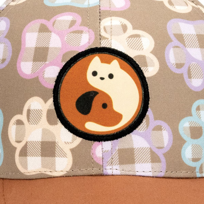 A cap featuring a light brown fabric with a playful paw print pattern and a circular patch displaying a cat and dog design.
