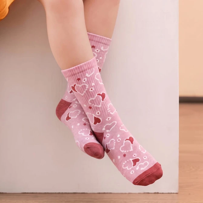A pair of pink knitted kids' socks featuring heart patterns and a reddish band at the top, resting on a white surface.