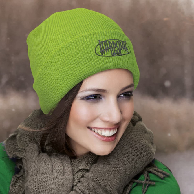 A vibrant green beanie with a ribbed texture, worn by a woman with a scarf in a winter setting.