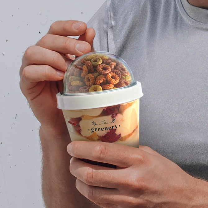 A drink bottle with a clear dome lid, featuring layered snacks and colourful cereal inside. It has a simple design and branding.
