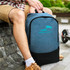 A blue and black backpack sits beside a person, featuring a logo on the front and a sleek design.