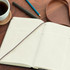 A large Moleskine Pro hard cover notebook with blank pages, a pen, pencil, and a coffee cup on a wooden surface.