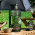 A drink bottle in transparent black with a sturdy handle, placed on a wooden table outdoors.