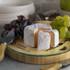 A bamboo cheese board featuring a round cheese, grapes, and a cheese knife, with a logo on the board.