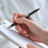 A hand holding a sleek black metal pen with a clip, poised over a clipboard and note paper.