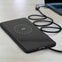 A black smartphone on a desk, charging wirelessly with a visible battery percentage. A charging cable is nearby.
