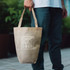 A small natural-coloured tote bag with handles, featuring a logo on the front.