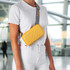A yellow Rollink Mini Bag Tour is worn across the body by a person in a bright, open space.
