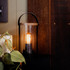 A black and transparent lantern with a wooden top, featuring a warm glowing bulb inside.