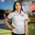 A girl wearing a white sports polo with red accents and a logo, standing in a sports setting.