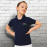 A navy blue kids' polo shirt featuring a logo on the left side, displayed on a girl against a brick wall backdrop.