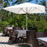 A white Café Umbrella with no valance stands above wicker outdoor tables and chairs among tropical greenery.