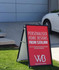 A black A-frame sign with a red insert promoting personalised home designs and featuring a logo, placed on green grass.