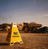 A yellow triangular signage stand marked "NO STOPPING" on a gravel surface, with mining trucks in the background.