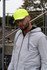 A man wearing a bright yellow cap with reflective trim and a grey hoodie stands in an outdoor setting.