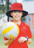 A boy in a red shirt wears a reversible breathable poly twill bucket hat with blue and red colours, holding a yellow volleyball.
