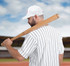 A man holds a wooden baseball bat over his shoulder, wearing a white striped shirt and a white cap.